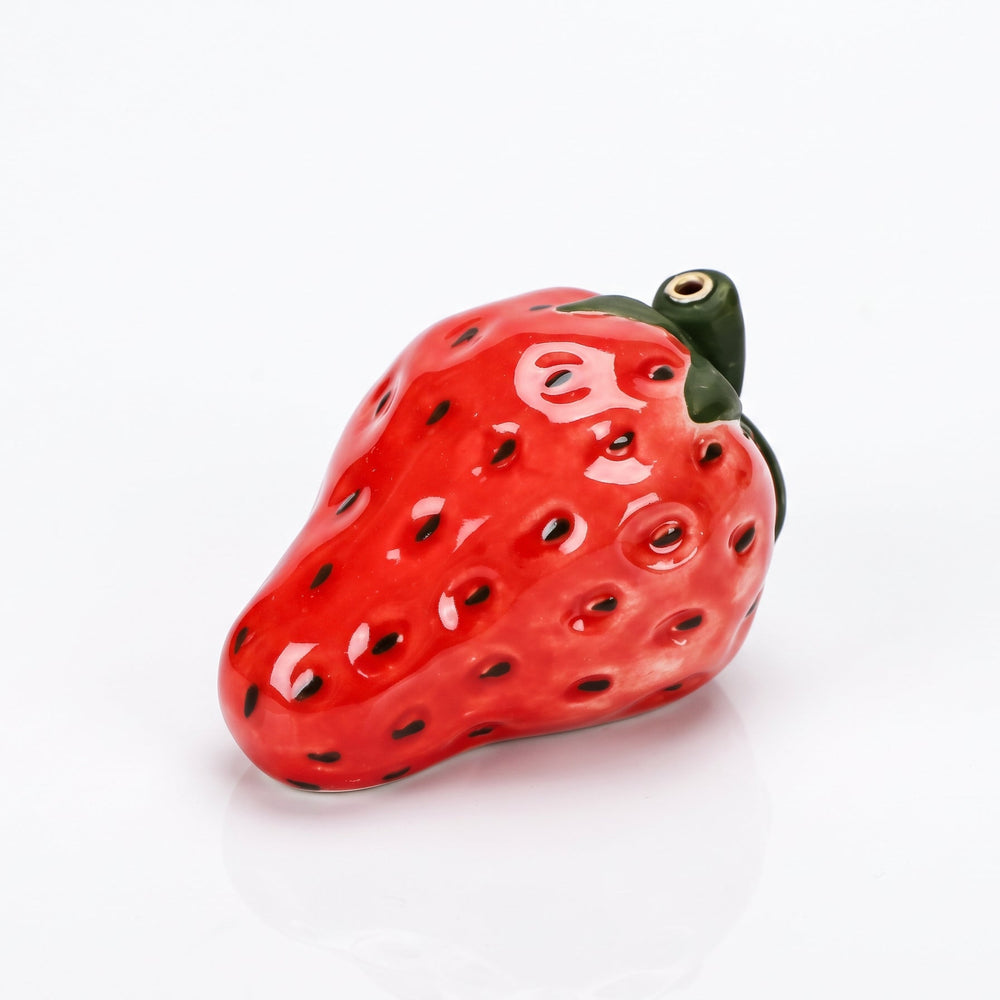 A glossy ceramic strawberry-shaped object, likely a candle holder or decorative figurine, featuring a vibrant red body with black seeds and a green stem, set against a plain white background.